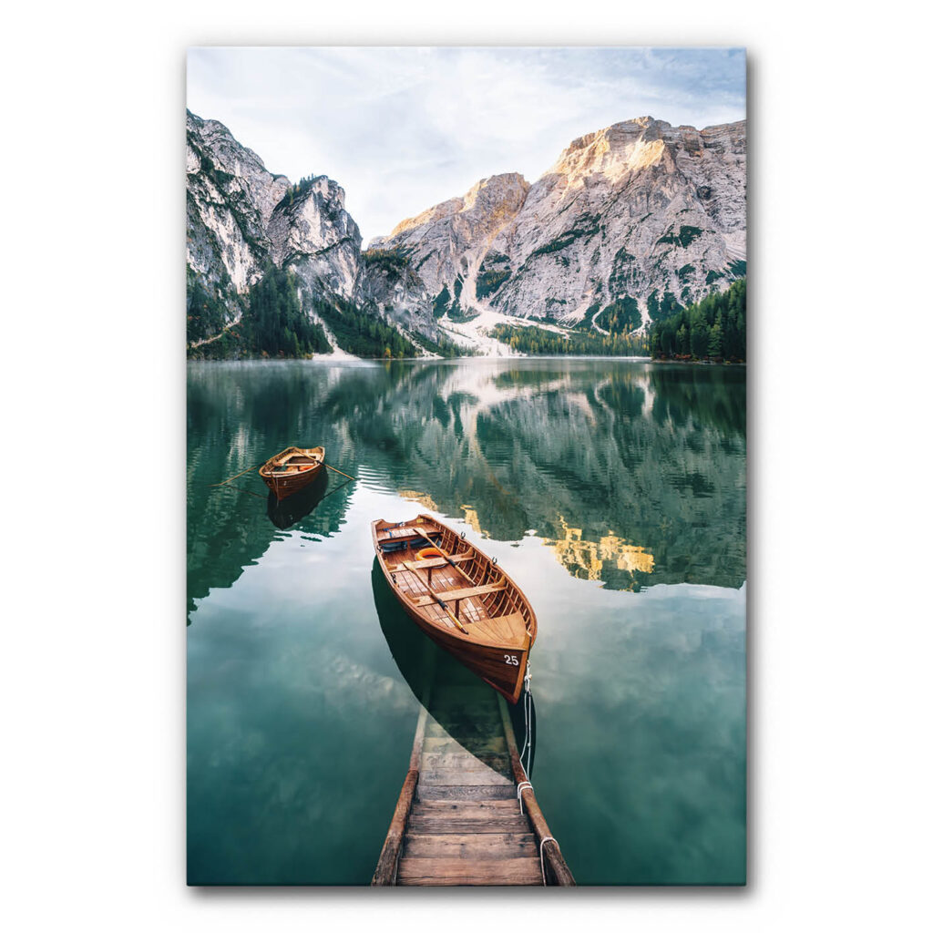 Schallabsorberbild Alpensee mit ruhigem Bergsee, zwei Holzbooten am Steg, spiegelnder Wasseroberfläche, umliegenden Bergen und klaren Blau- und Grüntönen, natürliches akustisch wirksames Wandbild.