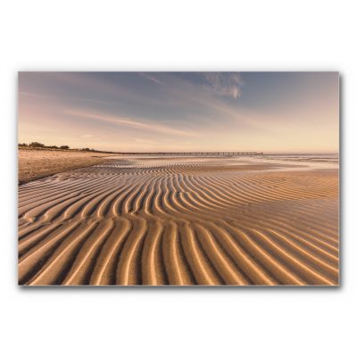Akustikbild Ostsee Strand zeigt eine ruhige Strandlandschaft bei sanftem Abendlicht, mit wellenförmig gezeichnetem Sand im Vordergrund und einem langen Steg, der sich bis zum Horizont über das Meer erstreckt.