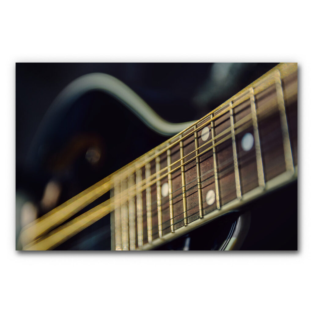 Akustikbild Guitar Strings - Perspektivische Detailaufnahme eines Guitarrenhalses in einer dunklen Stimmung mit goldenen Bundstäbchen und gold-schwarzen Saiten.